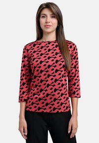 Red and black patterned top with a crew neckline, three-quarter sleeves, and a textured finish, paired with black pants.