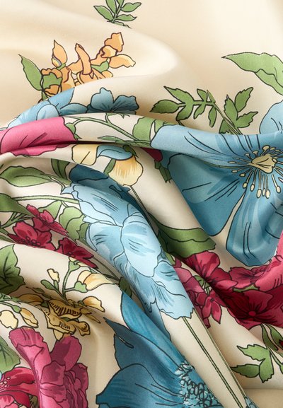 Tissu crème avec imprimé floral coloré comprenant des fleurs bleues, roses, jaunes et des feuilles vertes, présenté avec des plis doux et des rides.