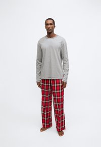 Pelēka krekla ar garām piedurknēm, kas kombinēta ar sarkaniem flaneļa pidžamas biksēm ar rūtiņu rakstu. Krekls ir brīva piegriezuma, savukārt bikses ir platām kājām un tartāna rakstā.