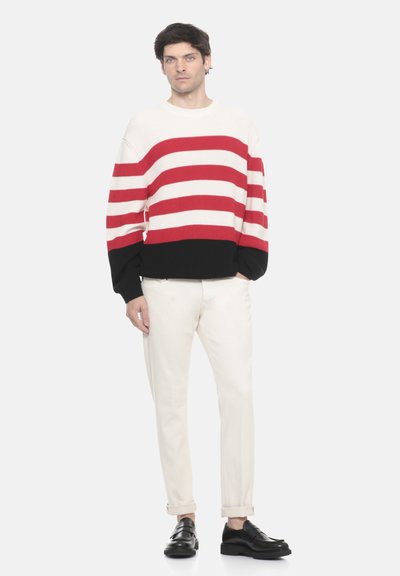 Maglione a righe in crema, rosso e nero. Tessuto a coste, vestibilità rilassata, con maniche lunghe. Abbinato a pantaloni crema e scarpe nere.