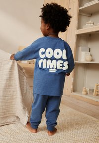 Ensemble de vêtements d'intérieur en coton bleu comprenant une chemise à manches longues avec un graphisme blanc "COOL TIMES" et un pantalon assorti avec des chevilles élastiquées.