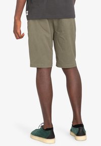 Olivgrön shorts i bomull, med regular fit och uppfälld fåll, kombinerade med gröna mockaskor och en grå skjorta.