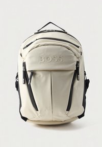 Beige ryggsekk i nylon med sorte detaljer, to frontlommer med glidelås, justerbare stropper og preget "BOSS"-logo på fronten.