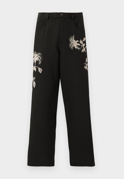 Musta leveälahkeinen housu, jossa on kermaisin sävyin tehtyä kukka-etikettiä. Siinä on etutaskut ja nappikiinnitys, ja se on valmistettu sileästä kankaasta.