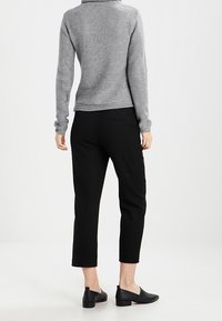 Suéter gris texturizado con un cuello alto, combinado con pantalones negros cortos y zapatos planos negros, visto desde la parte posterior.