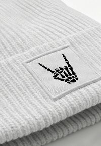 Gray knit beanie featuring a textured, ribbed design with a black embroidered patch of a skeletal hand symbol.