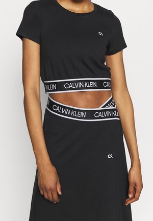 Kvinde iført en sort kort top og nederdel med hvide Calvin Klein elastiske taljebånd og korte ærmer.