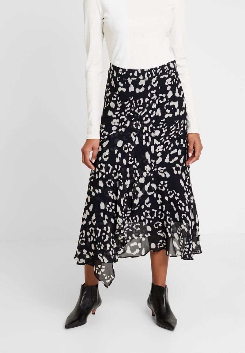 Jupe midi à imprimé léopard noir et blanc avec un ourlet fluide et asymétrique. Portée avec un top en côtes blanc et des bottines noires. 