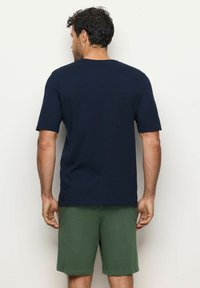 T-shirt di cotone blu navy con maniche corte, scollatura rotonda e vestibilità morbida, abbinato a pantaloni corti verdi. Design semplice, senza loghi visibili.