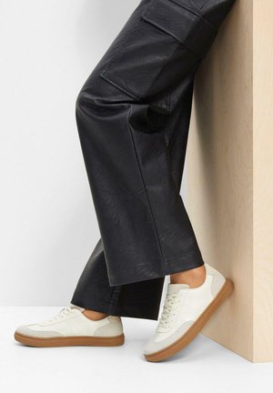 Baskets blanches avec un tissu texturé et des accents en cuir lisse, dotées d'une semelle en caoutchouc naturel, associées à un pantalon noir à jambes larges.
