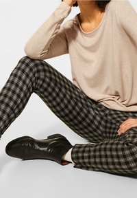 Vaaleanbeige pitkähihaiseen paitaan yhdistetty mustavalkoruudulliset housut. Asun täydentävät mustat nilkkurit.