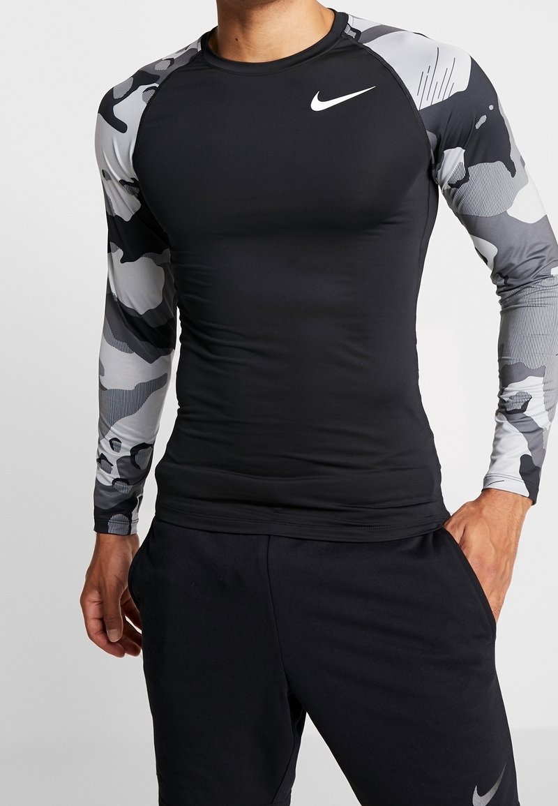 Długi rękaw koszulka sportowa, czarny korpus z rękawami w szarym wzorze moro, wykonana z elastycznego materiału, z logo Nike na piersi.