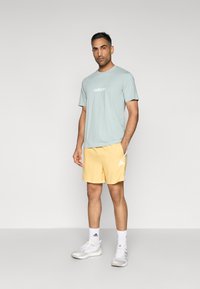 Heleroheline t-särk valge logoga, kombineeritud kollaste lühikeste pükstega, millel on kolm valget triipu. Valged spordijalatsid ja sokid lõpetavad komplekti.