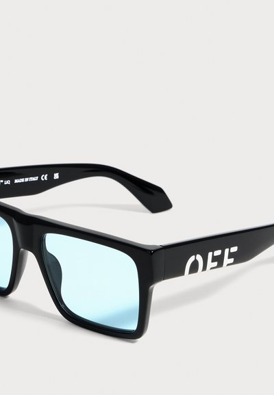 Lunettes de soleil rectangulaires noires avec des verres bleu clair et le mot « OFF » imprimé en blanc sur la branche droite.