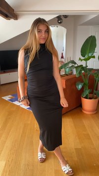Mustmustern ja musta, ilma varrukat dress, mis on väljakujunenud kujuga ja kortsudetailidega, koos valgete sandaalidega, millel on laia rihma disain.