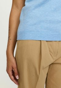 Svetlo modra pletena jopica in bež gubane hlače. Jopica ima rebrast rob, medtem ko imajo hlače gladko teksturo in vidne šive.