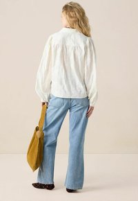 White embroidered blouse with puffed sleeves, paired with light blue flared jeans and a mustard yellow suede shoulder bag.