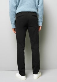 Zwarte broek met een op maat gemaakte pasvorm, voorzien van twee achterzakken en minimale stikdetails. Gecombineerd met witte sneakers en een lichtblauwe trui.