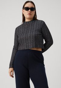 Black and silver ribbed knit cropped sweater with long sleeves, round neck, paired with dark navy ribbed pants, creating a coordinated outfit.
