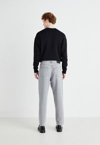 Black sweatshirt, grey denim pants, and black shoes. Sweatshirt has a round neck; pants are relaxed fit with back pockets and minimal detailing.
