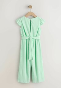 Combinaison courte à manches courtes vert menthe avec épaules à volants, ceinture en tissu, bouton dans le dos et jambes larges, suspendue à un cintre en bois.