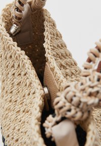 Geweven strohoed met een beige kleur en een textuurafwerking; heeft een soepele leren sluiting en een gevlochten handvat om te sluiten.