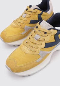 Sneaker in suede giallo e rete con dettagli blu navy, pannelli testurizzati e laccetti rotondi; presenta una spessa suola in gomma bianca.