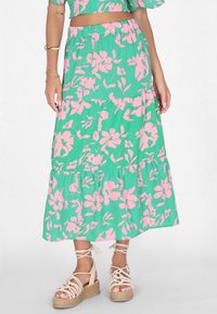 Gonna maxi in tessuto verde con stampa floreale rosa, design a strati e vita elasticizzata. Indossata con sandali espadrilles beige.