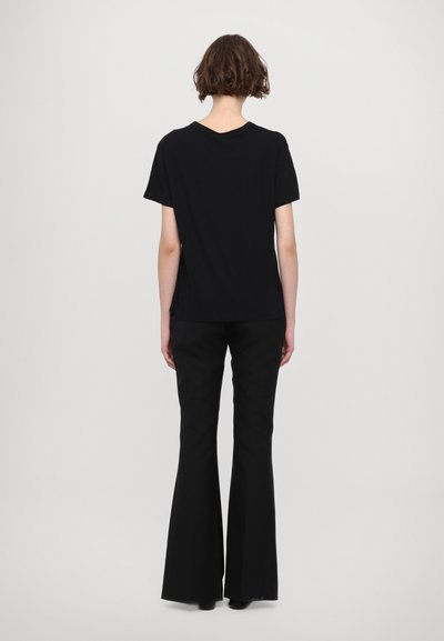 T-shirt noir à manches courtes en coton, accompagné de pantalons évasés noirs. La tenue est simple, sans motifs ni ornements visibles.