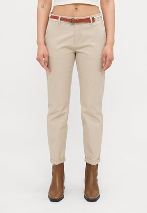 Pantaloni beige a sigaretta con risvolti, dotati di una cintura marrone. Tessuto morbido e design frontale piatto. Stivaletti marroni alla caviglia completano l'outfit.