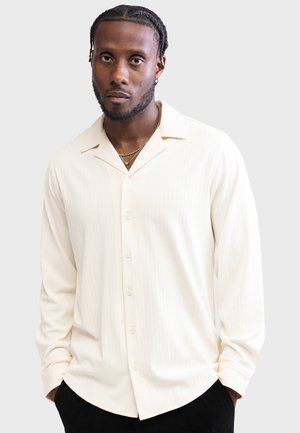 Cream-colored long-sleeve button-up shirt with subtle vertical stripes, a notched collar, and a relaxed fit. Flat buttons line the front.