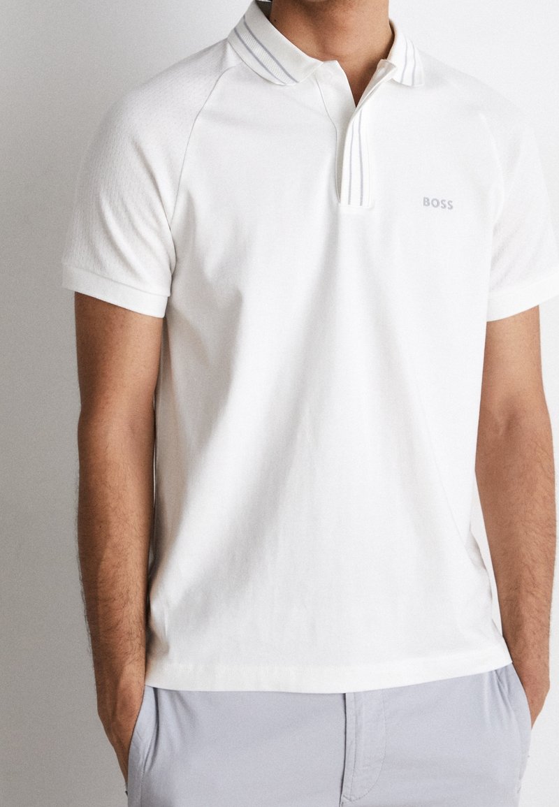 Polo blanc en tissu texturé. Col rayé et logo discret sur la poitrine. Manches courtes et coupe décontractée.