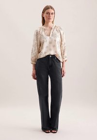 Blusa beige con motivo floreale e maniche a tre quarti, abbinata a pantaloni gris scuro ampi. Tessuto liscio e design casual.