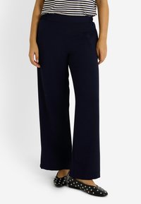 Pantalons larges en tissu bleu marine avec une finition texturée et une taille élastique, associés à des ballerines noires avec des clous en argent.