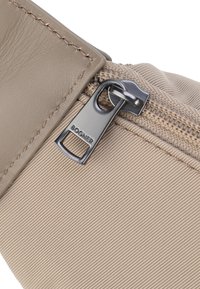 Borsa in tessuto beige con superficie texturizzata. Presenta una patta in pelle e una zip argento con il logo "Bogner". Dettagli cuciti lungo i bordi.
