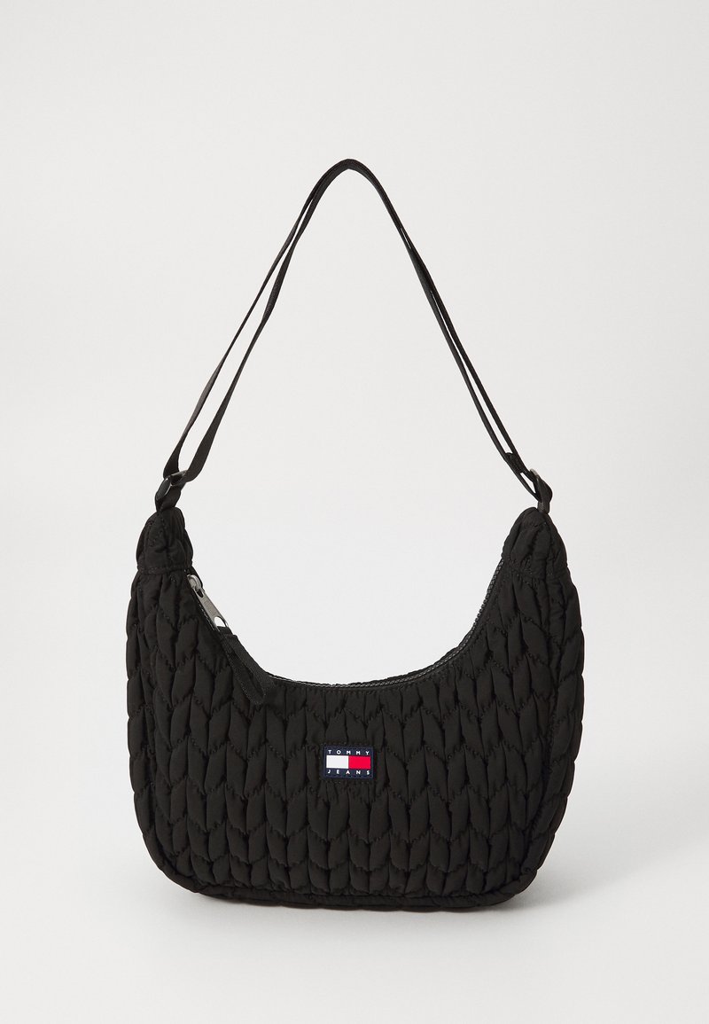 Svart vadderad handväska med en böjd form, utrustad med dragkedjestängning och en logotyp i rött, vitt och blått på framsidan. Två smala remmar.