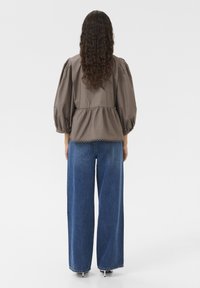 Braunes Oberteil mit Puffärmeln und Peplum-Saum sowie Spitze, kombiniert mit hoch taillierten, weit geschnittenen blauen Jeans.