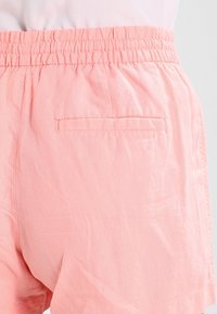 Shorts roses en tissu léger avec une taille élastique, dotés d'une poche arrière unique et d'une texture lisse.