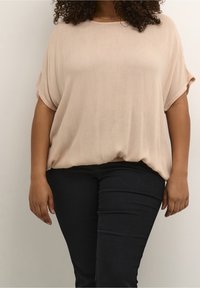 Losse korte mouwen top in lichtbeige, gemaakt van zacht, gestructureerd stof. Gecombineerd met zwarte slim-fit broek.