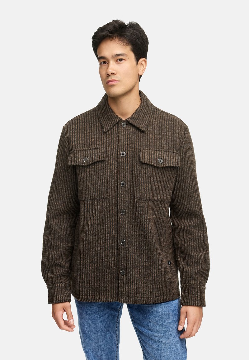 Brunrandig jacka med knäppning fram, två bröstfickor och klassisk krage. Tillverkad av strukturerad tyg, i kombination med blå jeans.