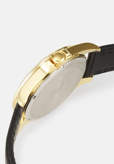 Aranyszínű óra, rozsdamentes acél házzal, fekete bőr szíjjal és kör alakú tok formával. Felhúzó koronát tartalmaz.