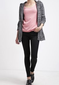 Grå stickad cardigan med huva över en rosa kortärmad topp, i kombination med tajta svarta jeans och svarta slipskor. Enkelt design.