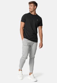Schwarzes T-Shirt mit kurzen Ärmeln und Logo, kombiniert mit hellgrauen, eng anliegenden Jogginghosen und weißen Sneakern. Glattes Material, lockere Passform, einfaches Design.