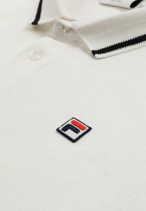 Polo blanc avec col rayé noir et blanc, boutons transparents, et petit logo carré brodé en noir, blanc et rouge sur la poitrine.
