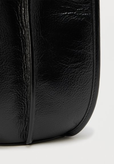 Μαύρη δερμάτινη τσάντα με ομαλή υφή, στρογγυλεμένο σχήμα και εμφανείς λεπτομέρειες ραφής. Διαθέτει μια ραφή κατά μήκος της μιας πλευράς.