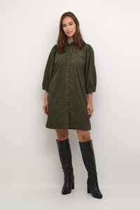 Olívzöld kordbársonydressz gombokkal, puffos ujjal és lezser fazonnal. Fekete, térd fölé érő magassarkú csizmával párosítva. Simasztjuk textura.