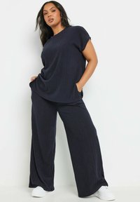 Laivansinisestä ribbimekosta koostuva kaksi osaa sisältävä kokonaisuus, jossa on lyhyet hihat, väljä paita ja leveät housut. Varustettu taskuilla ja yhdistetty valkoisiin lenkkareihin.