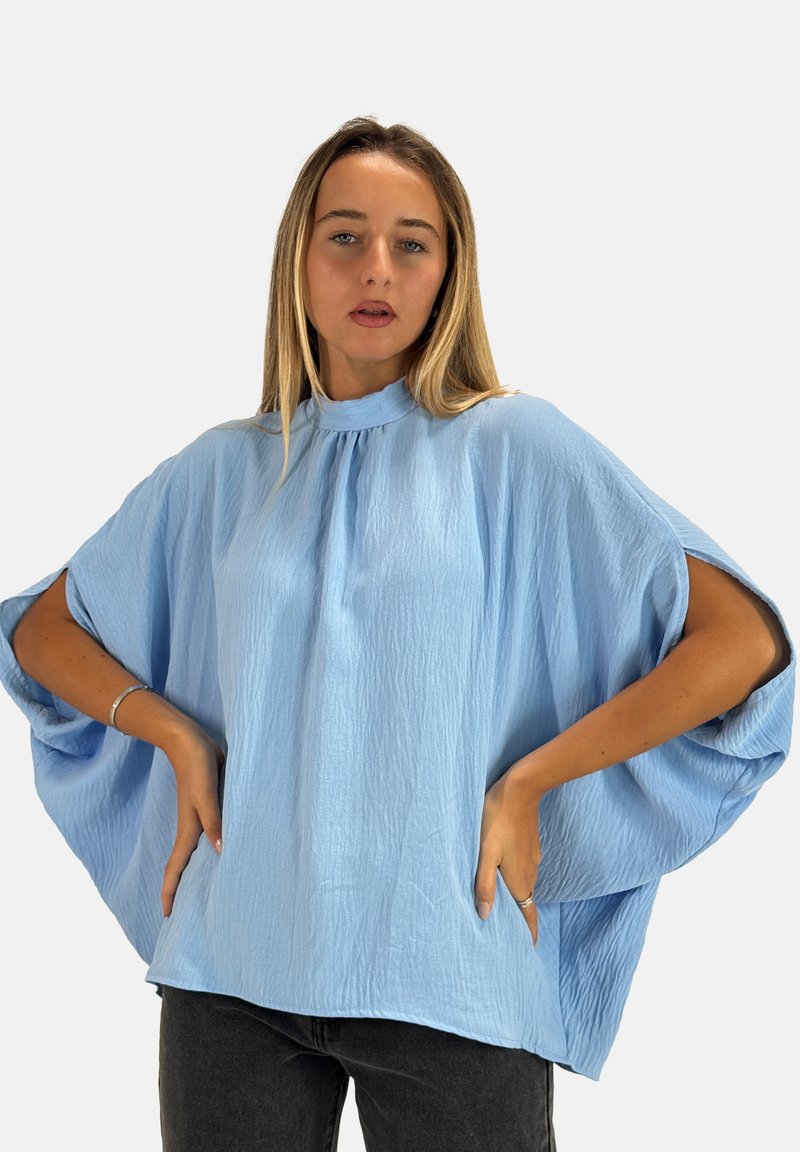Lyseblå, løs siddende top lavet af tekstureret stof, med en høj halsudskæring og brede ærmer, parret med mørke jeans.