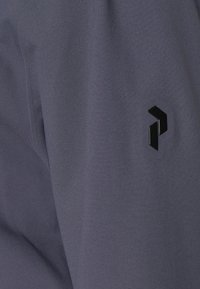 Tissu gris à texture lisse présentant un logo géométrique noir sur le côté gauche. Design minimaliste avec des lignes épurées.