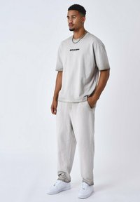 Camiseta de algodón gris claro de manga corta con un logo negro, combinada con pantalones de chándal gris claro a juego y zapatillas blancas.